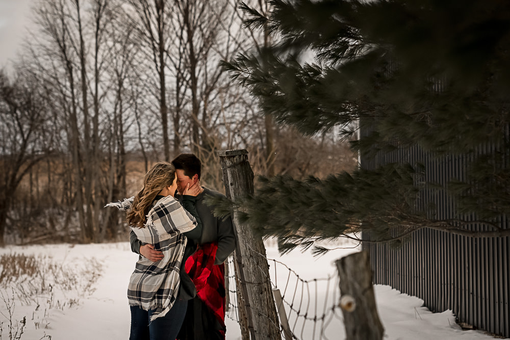 couple snuggling again wood fence at winter engagement session in Owen Sound