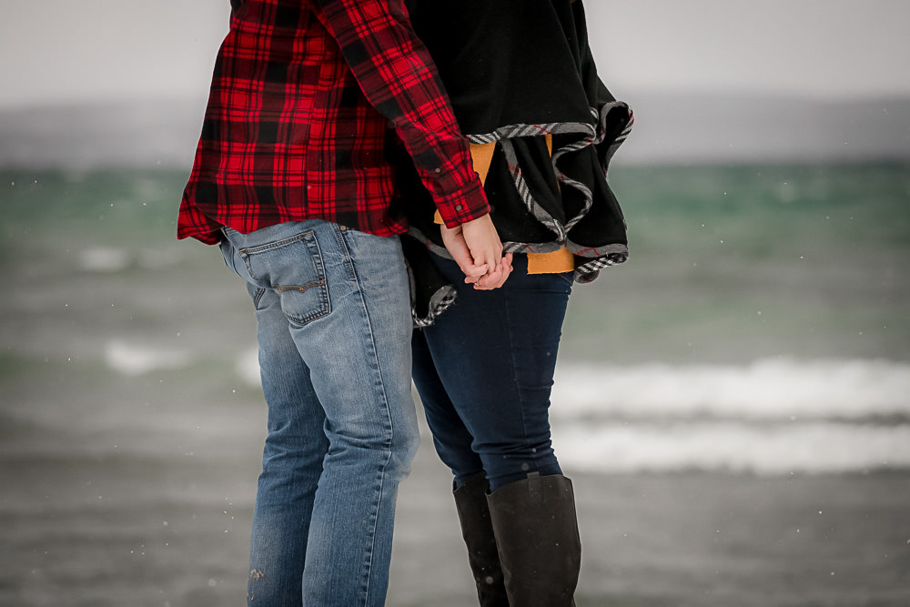 holding hands by the waterfront in Owen Sound with the waves crashing behind them.